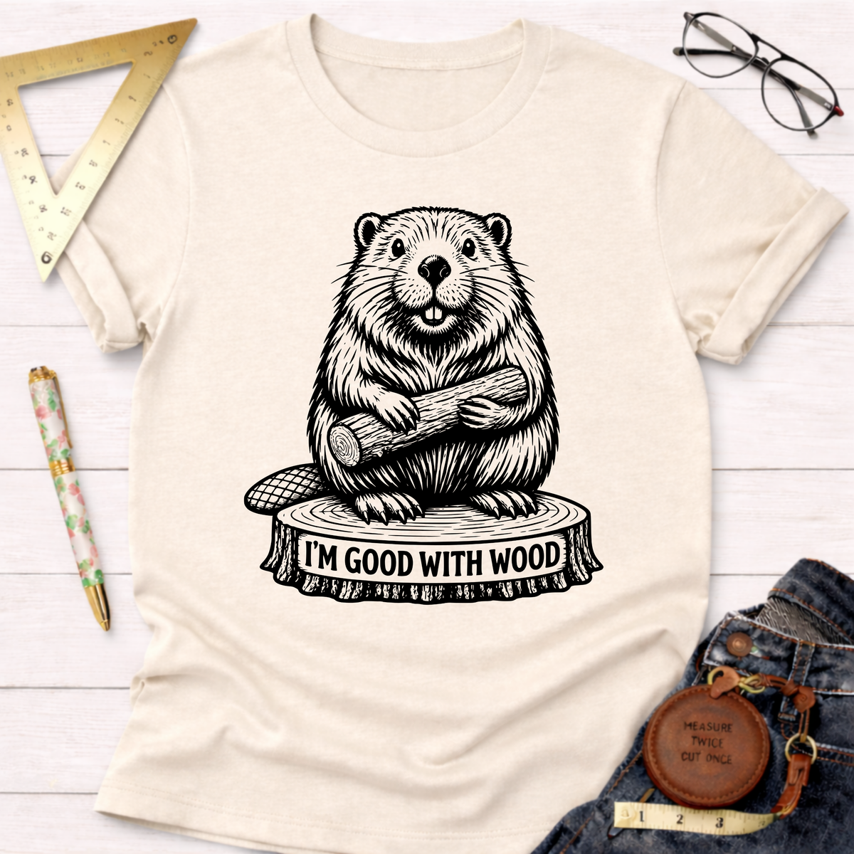 Women's funny woodworking graphic tee shirt for female woodworkers, makers, and DIY builders — Sawdust & Ponytails. Cream t-shirt with a black beaver holding wood on a tree stump graphic.