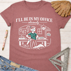 Women's funny woodworking graphic tee shirt for female woodworkers, makers, and DIY builders — Sawdust & Ponytails. Mauve cotton t-shirt with "I'll Be In My Office" text and a cartoon woman sawing wood.