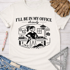 Women's funny woodworking graphic tee shirt for female woodworkers, makers, and DIY builders — Sawdust & Ponytails. Cream t-shirt with "I'll Be In My Office Obviously" text and a graphic of a woman in a woodshop.
