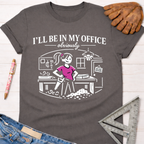 Women's funny woodworking graphic tee shirt for female woodworkers, makers, and DIY builders — Sawdust & Ponytails. Dark gray t-shirt with "I'll be in my office - obviously" and a cartoon woman sawing wood.