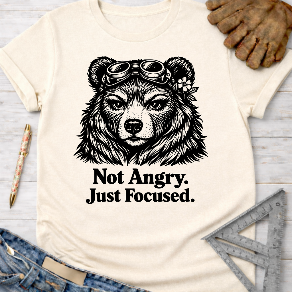 Women's funny woodworking graphic tee shirt for female woodworkers, makers, and DIY builders — Sawdust & Ponytails. Cream t-shirt with a black bear wearing goggles and the text "Not Angry. Just Focused.