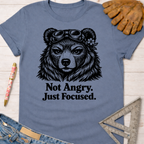 Women's funny woodworking graphic tee shirt for female woodworkers, makers, and DIY builders — Sawdust & Ponytails. Blue cotton tee with a focused bear in goggles and "Not Angry. Just Focused." text.
