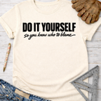 Cream "DO IT YOURSELF so you know who to blame" graphic tee, with jeans, work glove, pen, and ruler. Women's funny woodworking graphic tee shirt for female woodworkers, makers, and DIY builders — Sawdust & Ponytails