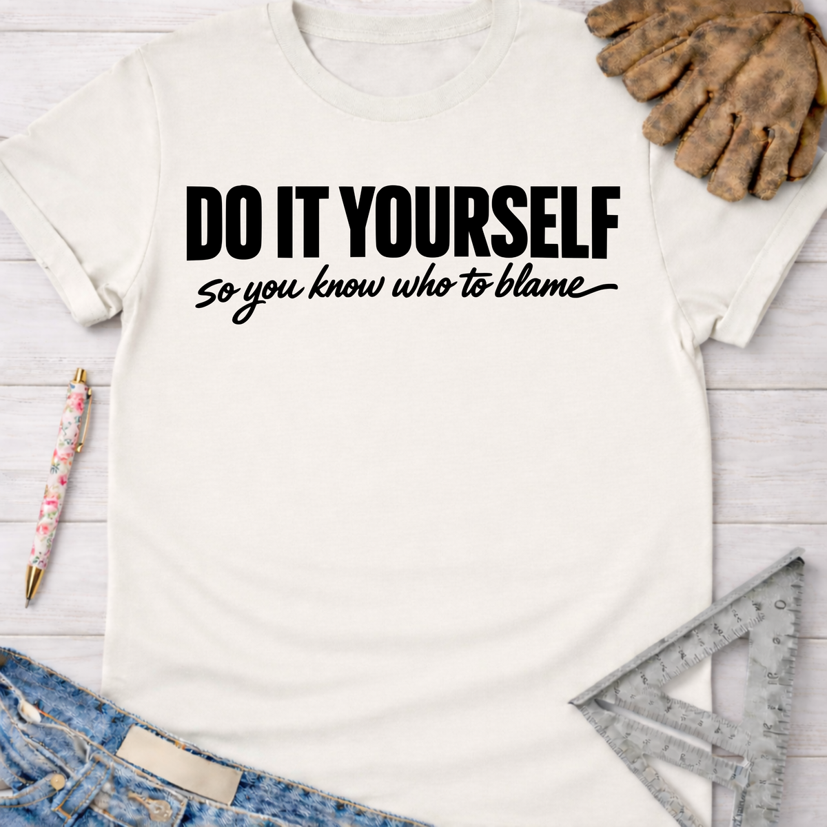Women's funny woodworking graphic tee shirt for female woodworkers, makers, and DIY builders — Sawdust & Ponytails. White cotton t-shirt with "DO IT YOURSELF so you know who to blame" in black text.