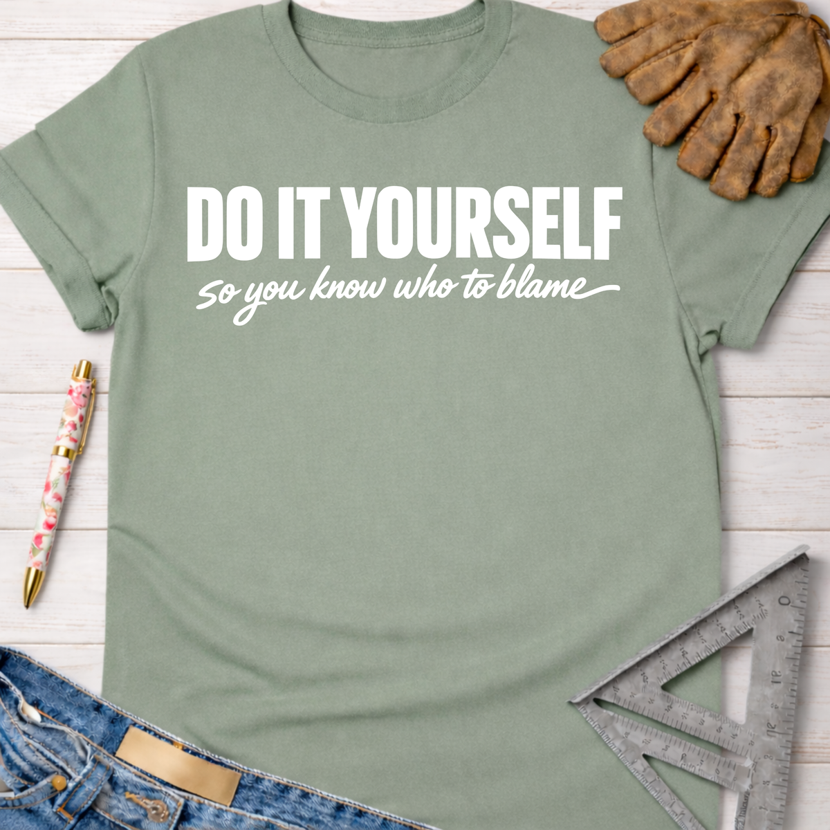Women's funny woodworking graphic tee shirt for female woodworkers, makers, and DIY builders — Sawdust & Ponytails. Sage green t-shirt with "DO IT YOURSELF so you know who to blame" in white text.