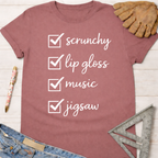 Women's funny woodworking graphic tee shirt for female woodworkers, makers, and DIY builders — Sawdust & Ponytails. Mauve t-shirt with "scrunchy, lip gloss, music, jigsaw" checklist.