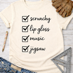 Women's funny woodworking graphic tee shirt for female woodworkers, makers, and DIY builders — Sawdust & Ponytails. Cream t-shirt with "scrunchy, lip gloss, music, jigsaw" checklist design.