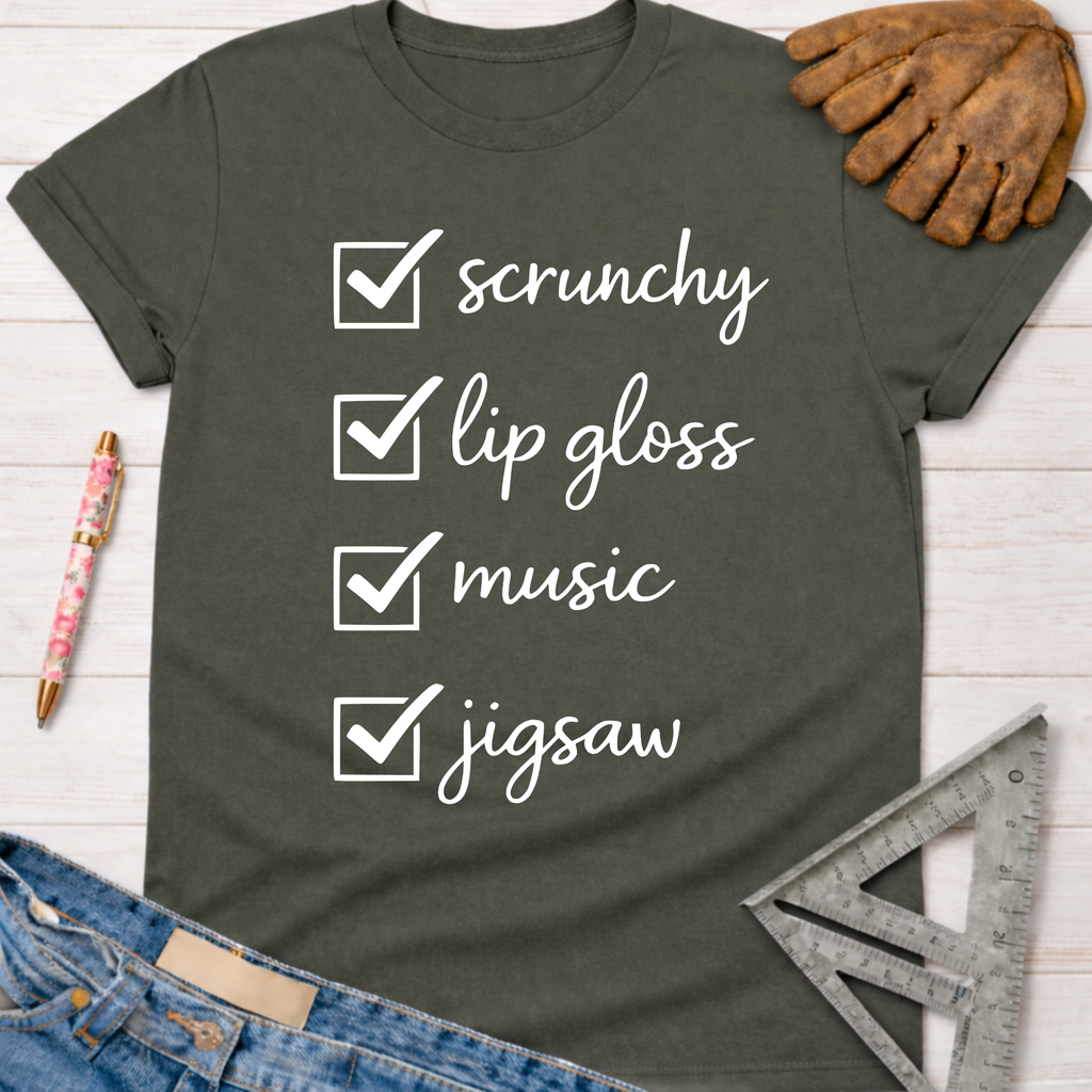 Women's funny woodworking graphic tee shirt for female woodworkers, makers, and DIY builders — Sawdust & Ponytails. Dark gray t-shirt with "scrunchy, lip gloss, music, jigsaw" checklist.