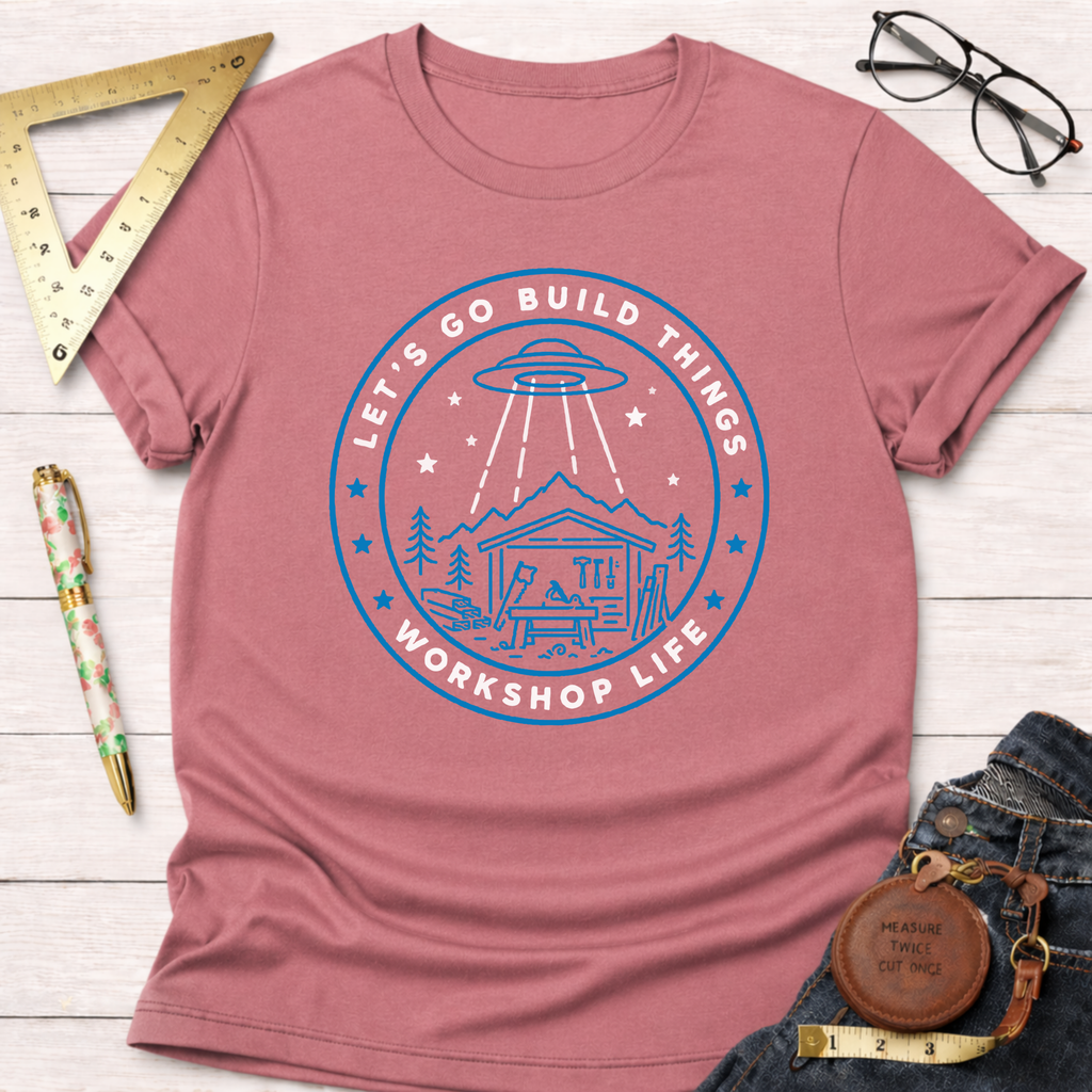 Pink "Let's Go Build Things Workshop Life" t-shirt with a blue graphic of a workshop and UFO.