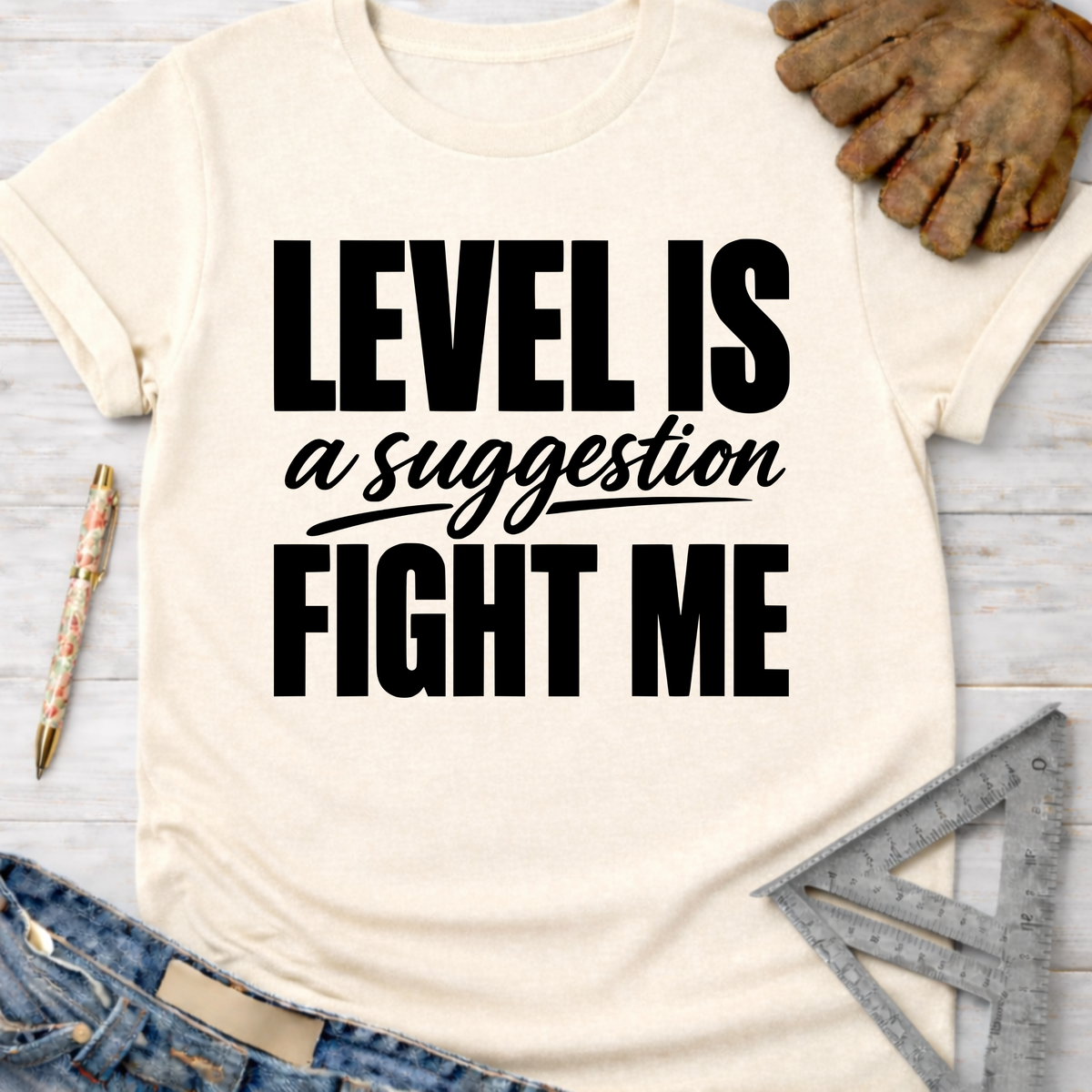 Cream t-shirt with "LEVEL IS a suggestion FIGHT ME" in black text, styled with jeans, work gloves, and tools. Women's funny woodworking graphic tee shirt for female woodworkers, makers, and DIY builders — Sawdust & Ponytails.