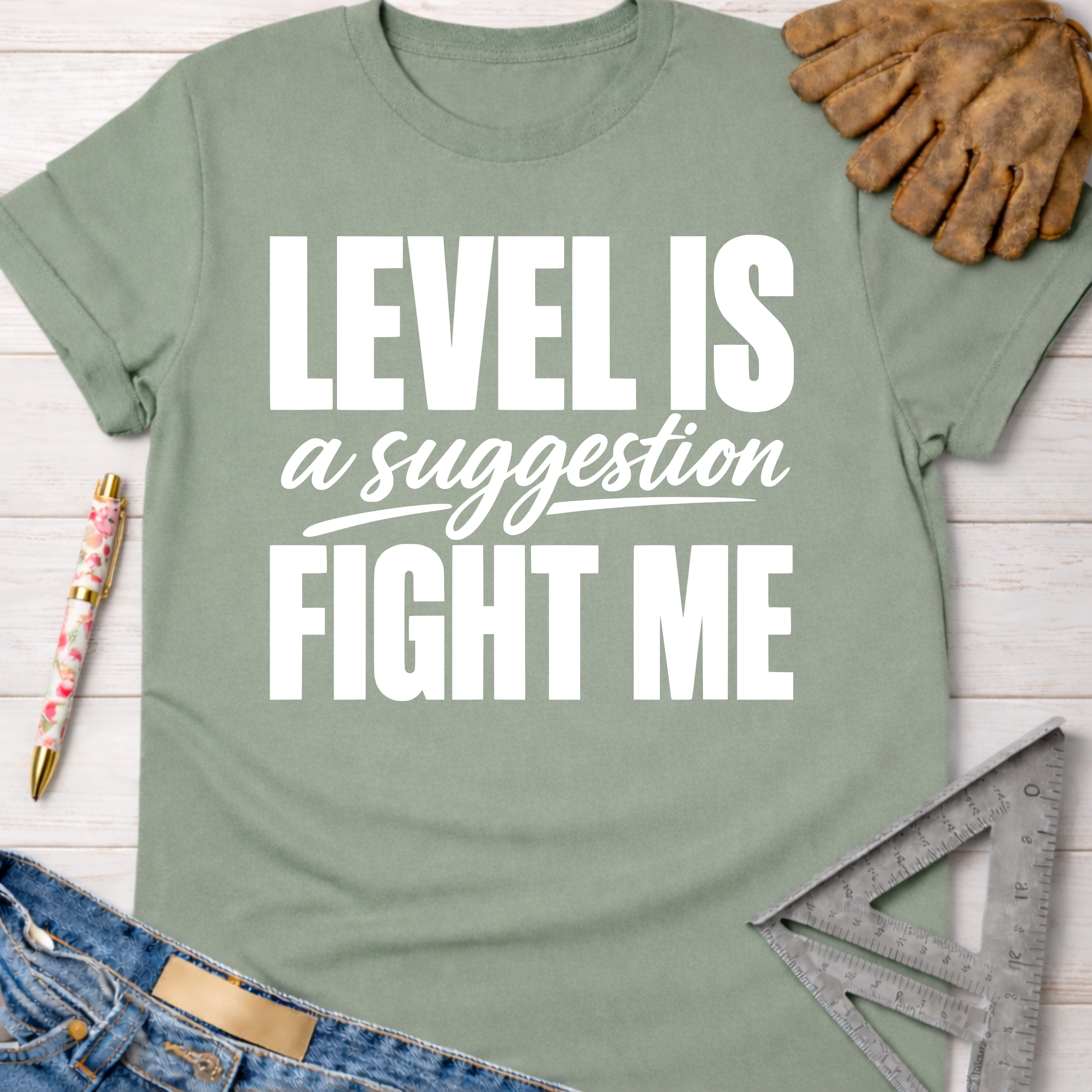 Sage green women's "Level Is A Suggestion FIGHT ME" t-shirt with white text, denim, and work gloves.
