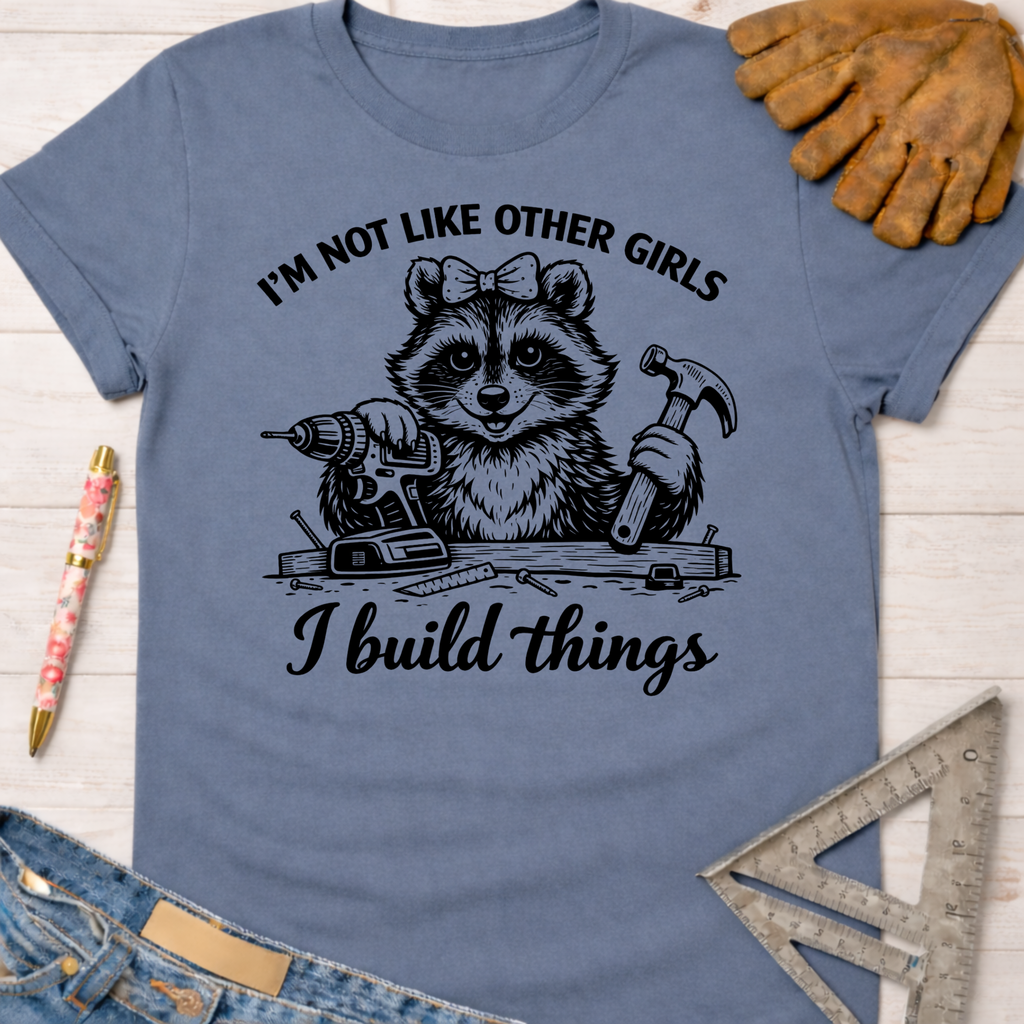 Women's funny woodworking graphic tee shirt for female woodworkers, makers, and DIY builders — Sawdust & Ponytails. Blue tee with a raccoon holding a drill and hammer, "I'm not like other girls, I build things" text.