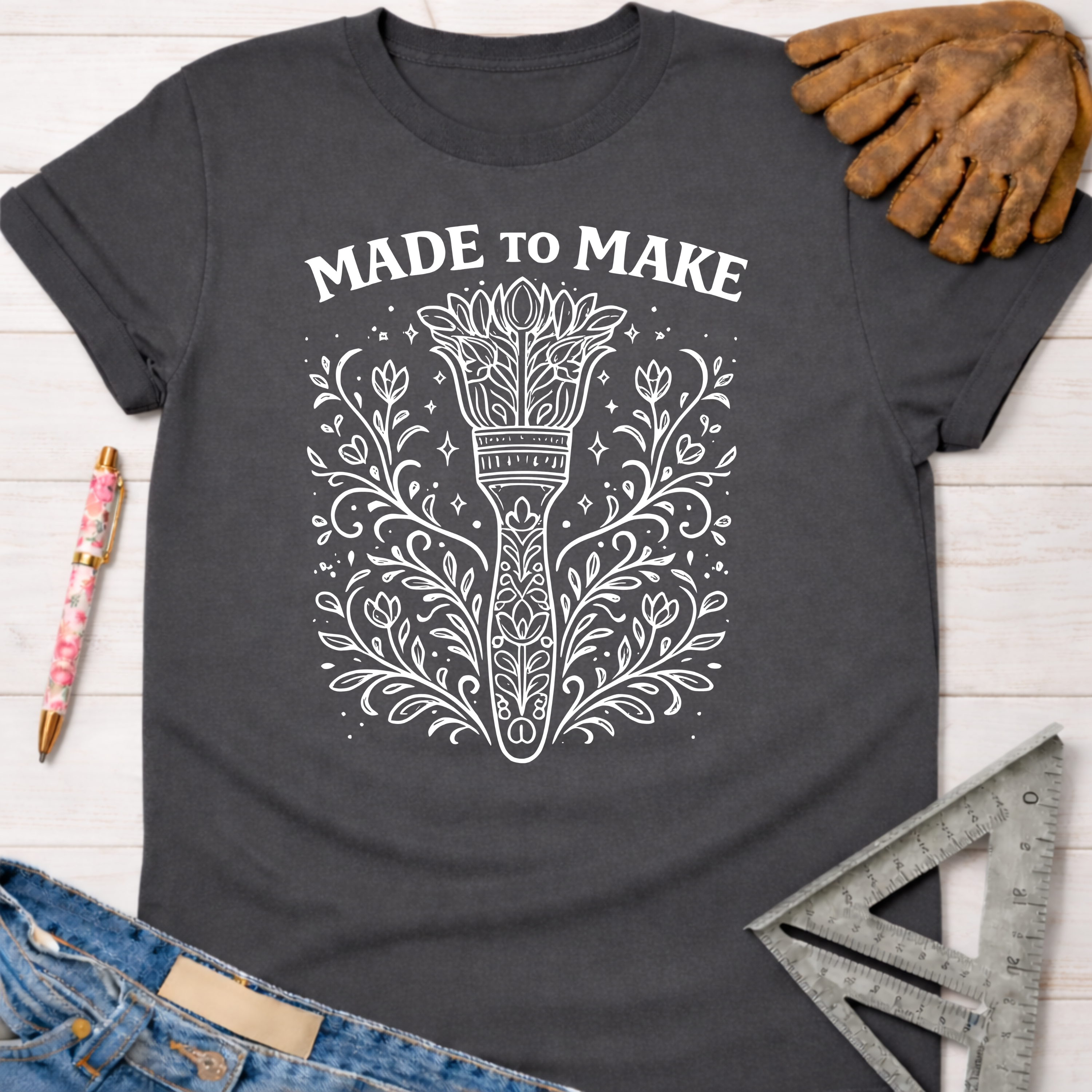 Women's funny woodworking graphic tee shirt for female woodworkers, makers, and DIY builders — Sawdust & Ponytails. Dark gray cotton tee with "MADE TO MAKE" and a floral paintbrush design.