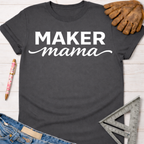 Charcoal gray "Maker mama" graphic tee with white text, denim, a pen, and work glove. Women's funny woodworking graphic tee shirt for female woodworkers, makers, and DIY builders — Sawdust & Ponytails.