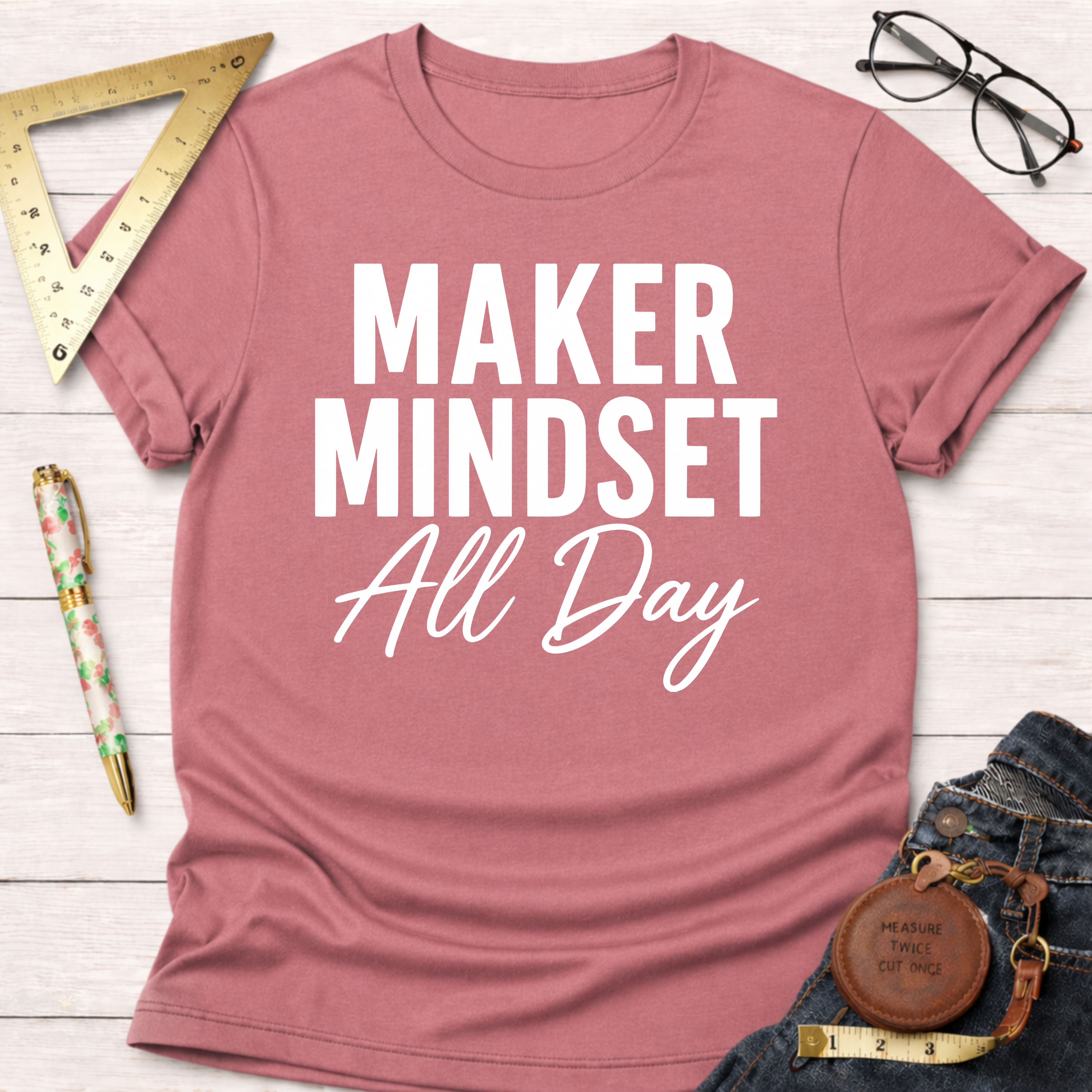Pink cotton t-shirt with "MAKER MINDSET All Day" in white text, styled with jeans and tools.