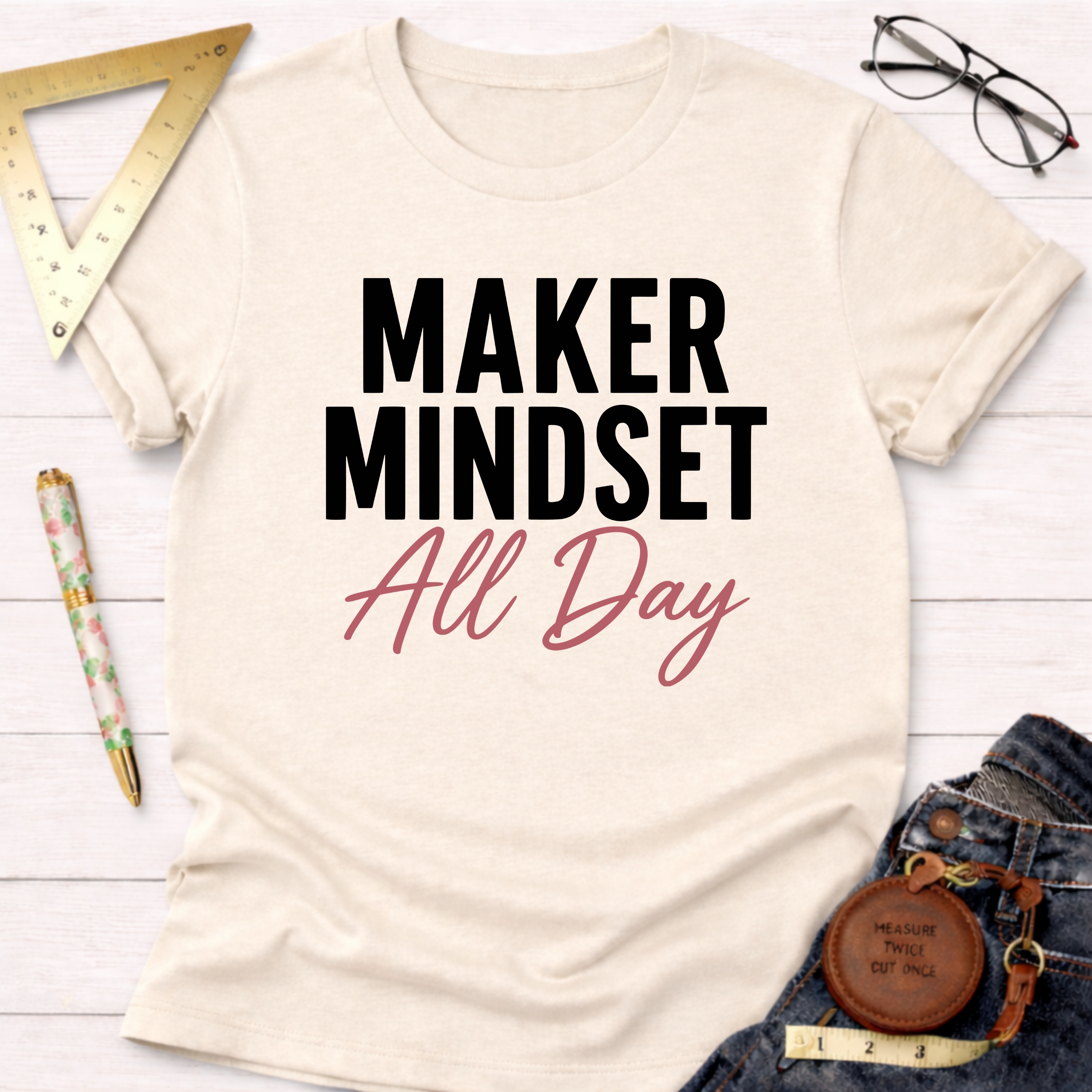Cream "Maker Mindset All Day" graphic t-shirt with black and pink text, styled with jeans and tools.