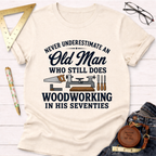 Cream t-shirt with "Never Underestimate An Old Man Who Still Does Woodworking In His Seventies" text and tools.
