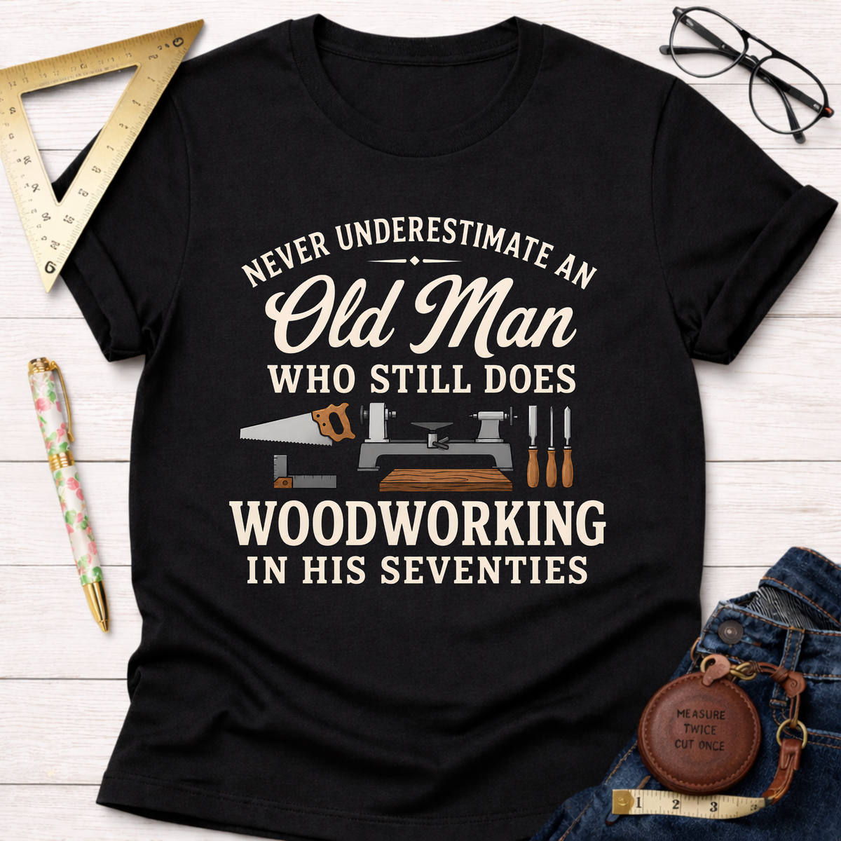 Black cotton t-shirt with "Never Underestimate An Old Man Who Still Does Woodworking In His Seventies" text and tools graphic.