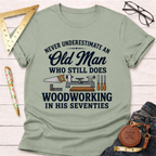 Sage green t-shirt with "Never Underestimate An Old Man Who Still Does Woodworking In His Seventies" text and tools.