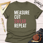 Olive green t-shirt with "MEASURE CUT SWEAR REPEAT" in white and pink text, styled with jeans and tools.
