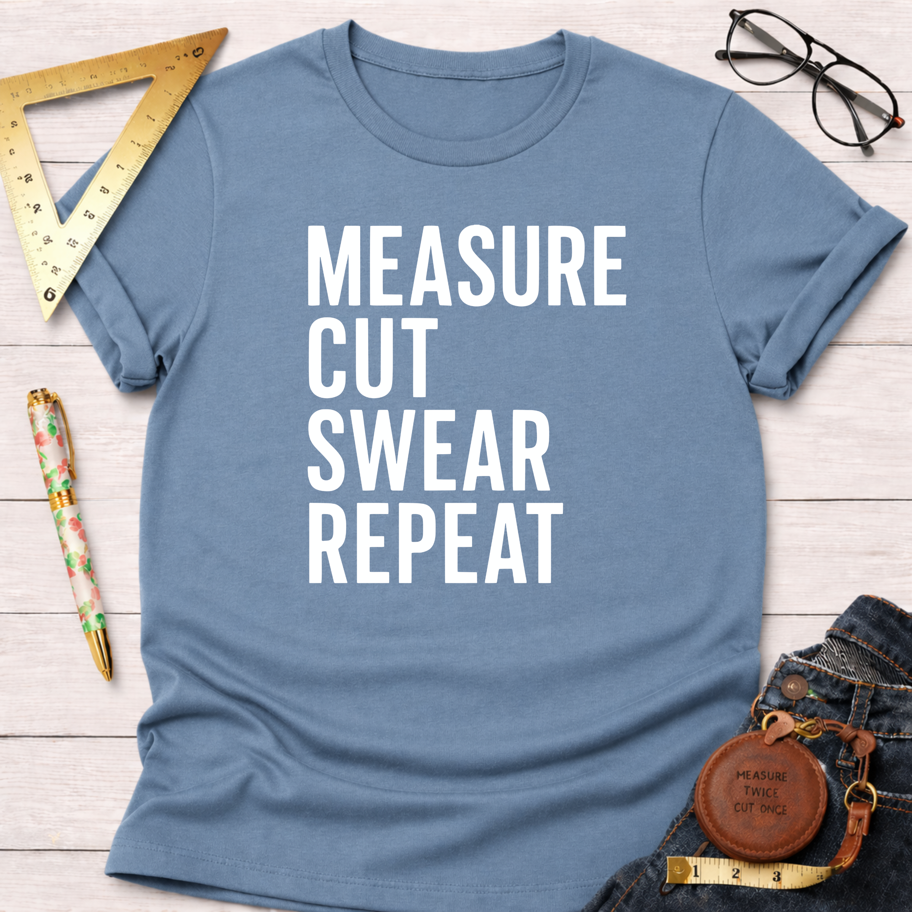Blue cotton t-shirt with "MEASURE CUT SWEAR REPEAT" in white text, styled with jeans and tools.