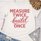 Women's funny woodworking graphic tee shirt for female woodworkers, makers, and DIY builders — Sawdust & Ponytails. White cotton tee with "Measure Twice build Once" in pink text.