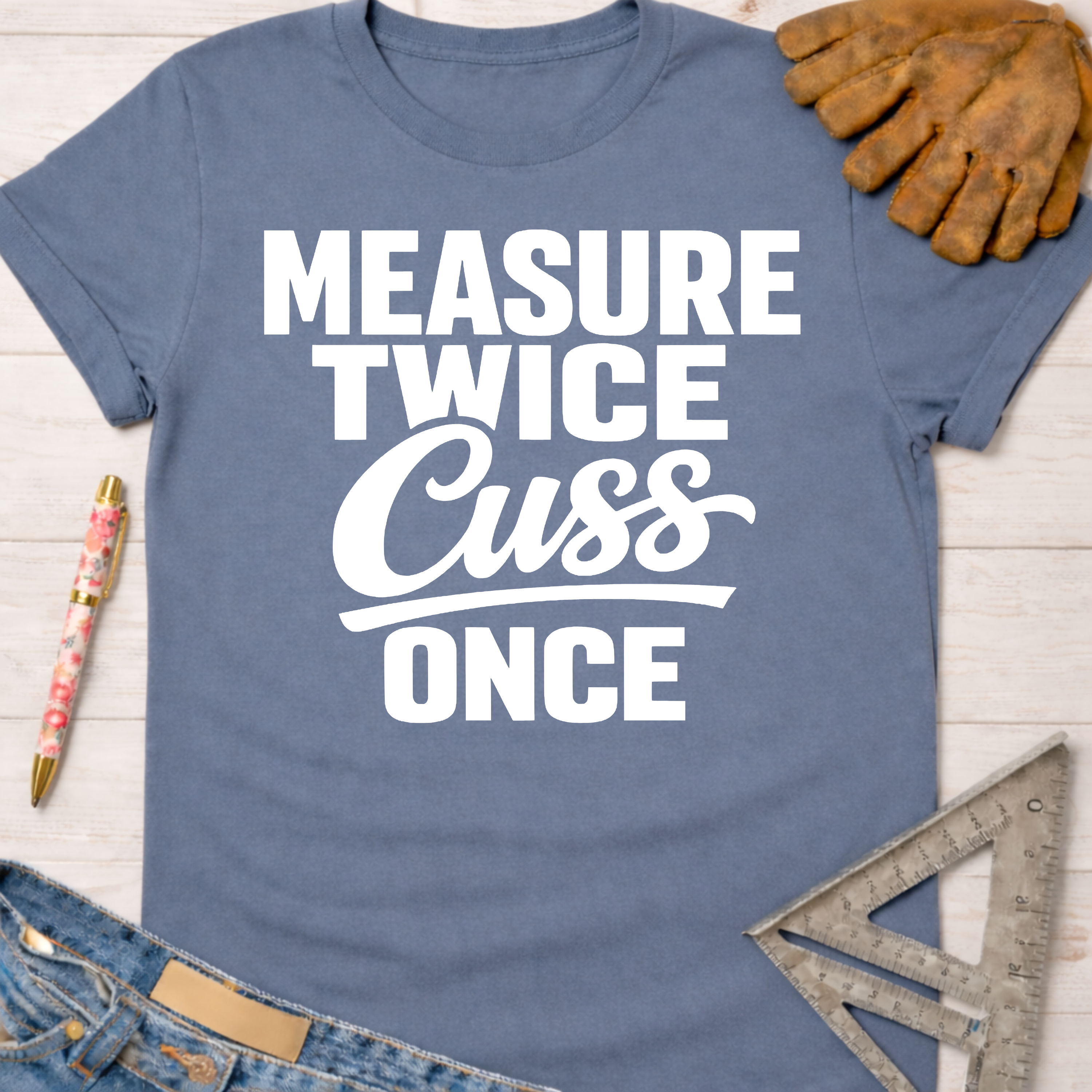 Women's funny woodworking graphic tee shirt for female woodworkers, makers, and DIY builders — Sawdust & Ponytails. Blue crew neck t-shirt with "Measure Twice Cuss Once" in white text.