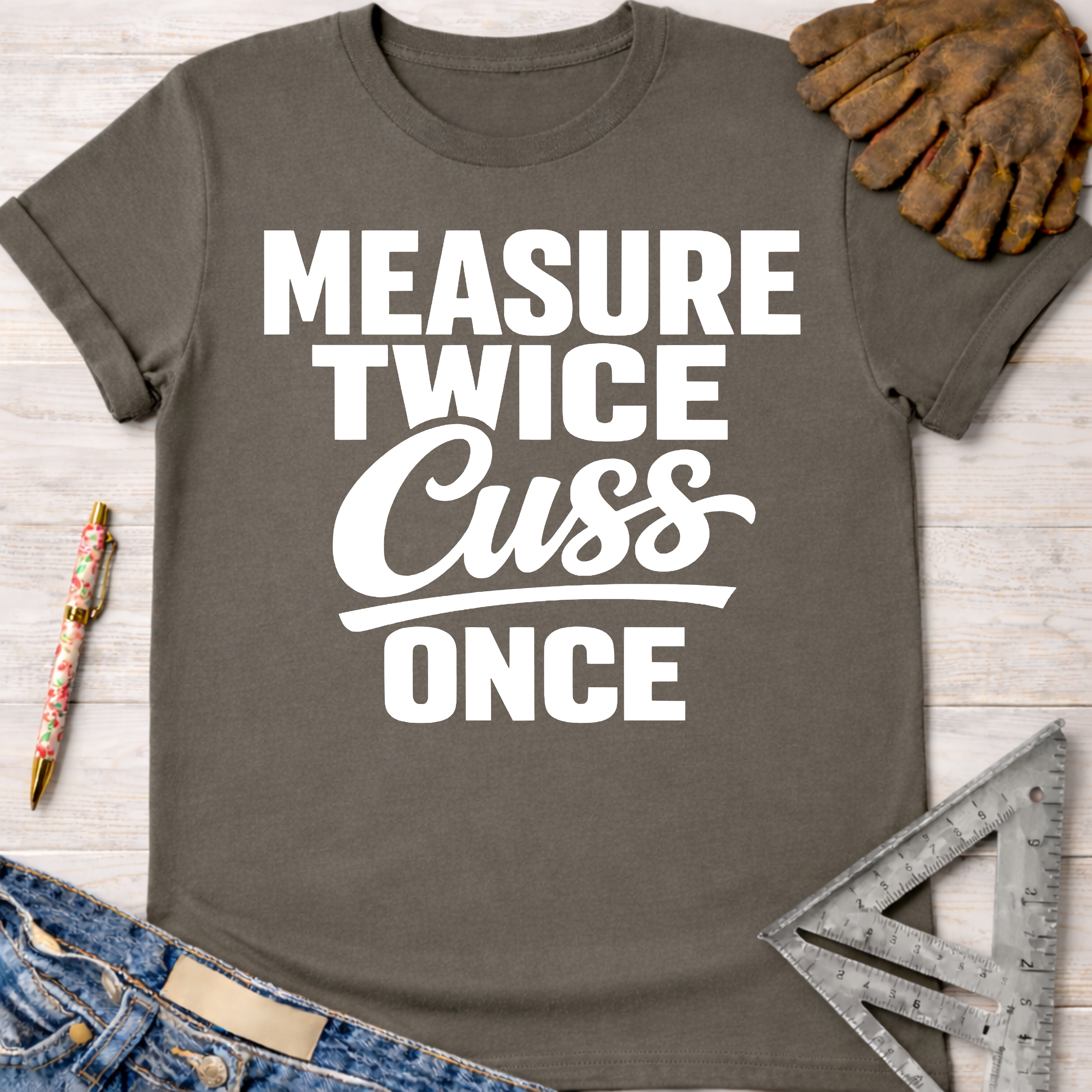 Women's funny woodworking graphic tee shirt for female woodworkers, makers, and DIY builders — Sawdust & Ponytails. Dark gray cotton t-shirt with "Measure Twice Cuss Once" in white text.