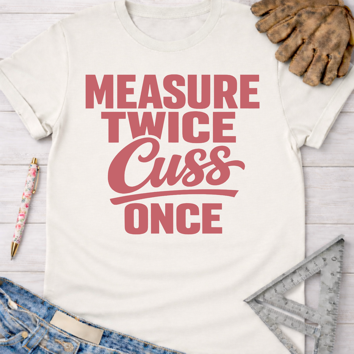 Women's funny woodworking graphic tee shirt for female woodworkers, makers, and DIY builders — Sawdust & Ponytails. White cotton tee with "Measure Twice Cuss Once" in pink text.