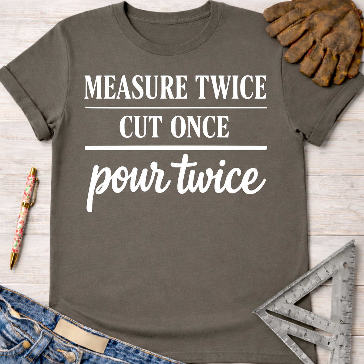 Women's funny woodworking graphic tee shirt for female woodworkers, makers, and DIY builders — Sawdust & Ponytails. Dark gray short-sleeve t-shirt with "MEASURE TWICE CUT ONCE pour twice" in white text.