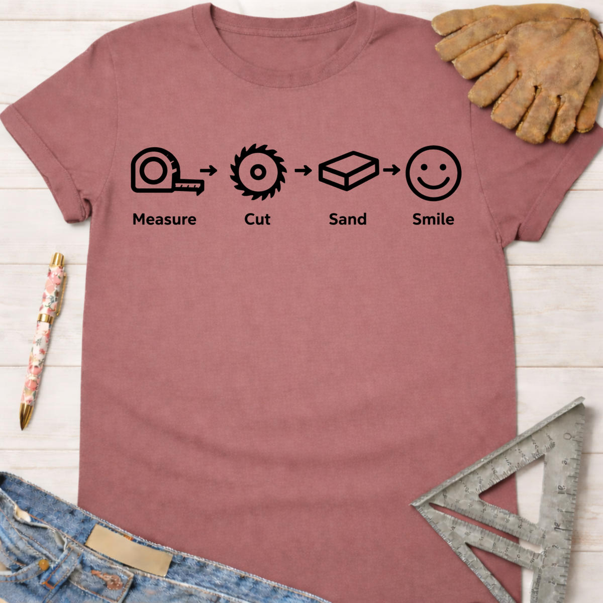 Women's funny woodworking graphic tee shirt for female woodworkers, makers, and DIY builders — Sawdust & Ponytails. Mauve cotton t-shirt with "Measure. Cut. Sand. Smile." icons.