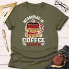Olive green t-shirt with "Measuring In Coffee Cups" text and a coffee mug wrapped in a measuring tape graphic.