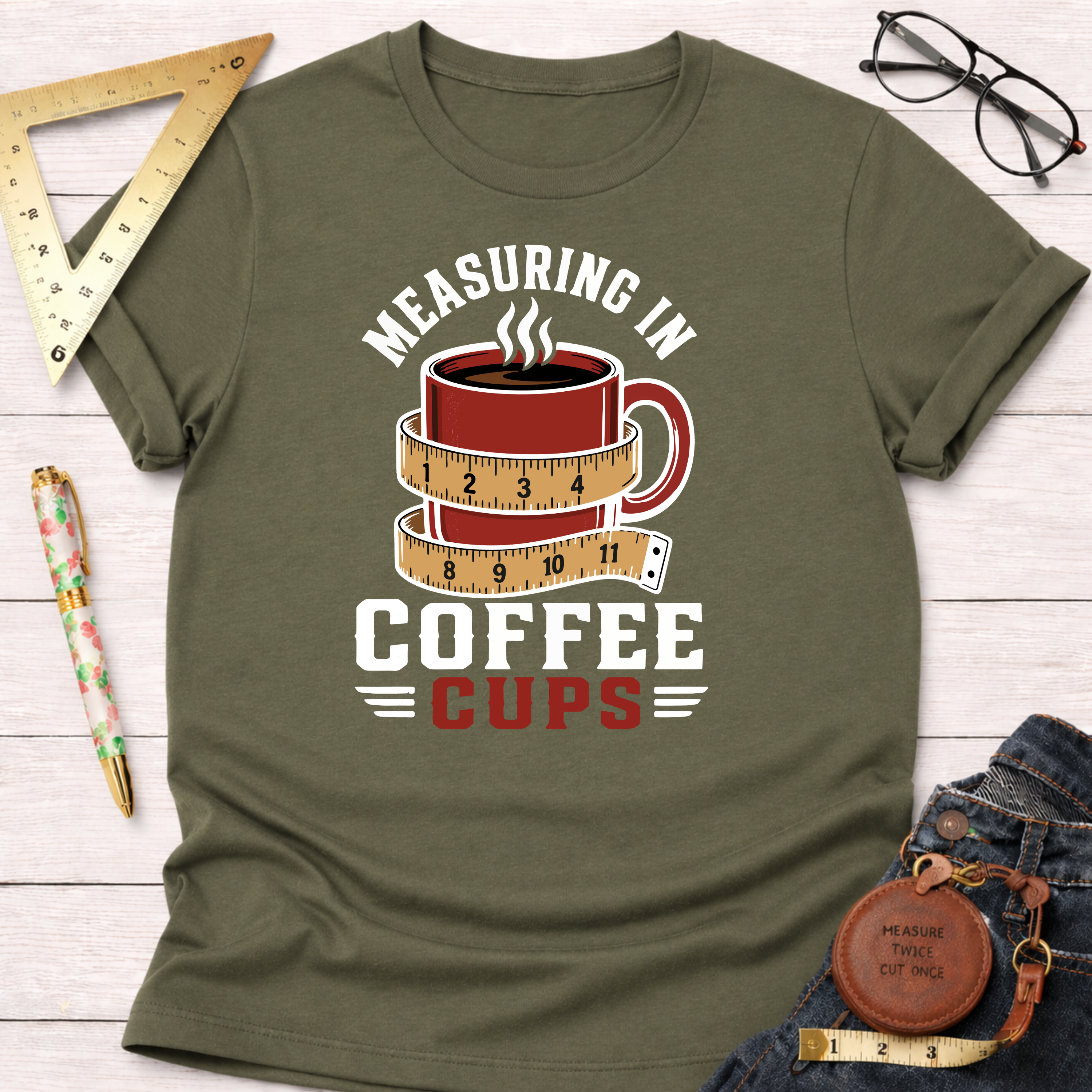Olive green t-shirt with "Measuring In Coffee Cups" text and a coffee mug wrapped in a measuring tape graphic.