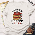 White cotton t-shirt with a red coffee mug wrapped in a measuring tape design and "Measuring In Coffee Cups" text.