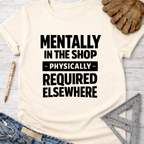 Women's funny woodworking graphic tee shirt for female woodworkers, makers, and DIY builders — Sawdust & Ponytails. Cream t-shirt with "Mentally In The Shop - Physically - Required Elsewhere" in black text.