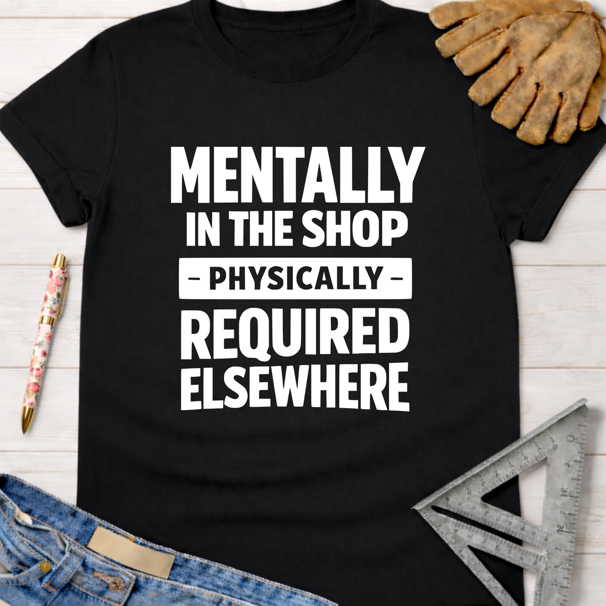 Black cotton tee with "MENTALLY IN THE SHOP - PHYSICALLY - REQUIRED ELSEWHERE" in white text. Women's funny woodworking graphic tee shirt for female woodworkers, makers, and DIY builders — Sawdust & Ponytails