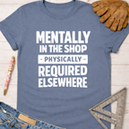 Women's funny woodworking graphic tee shirt for female woodworkers, makers, and DIY builders — Sawdust & Ponytails. Blue cotton tee with "Mentally In The Shop - Physically - Required Elsewhere" in white text.