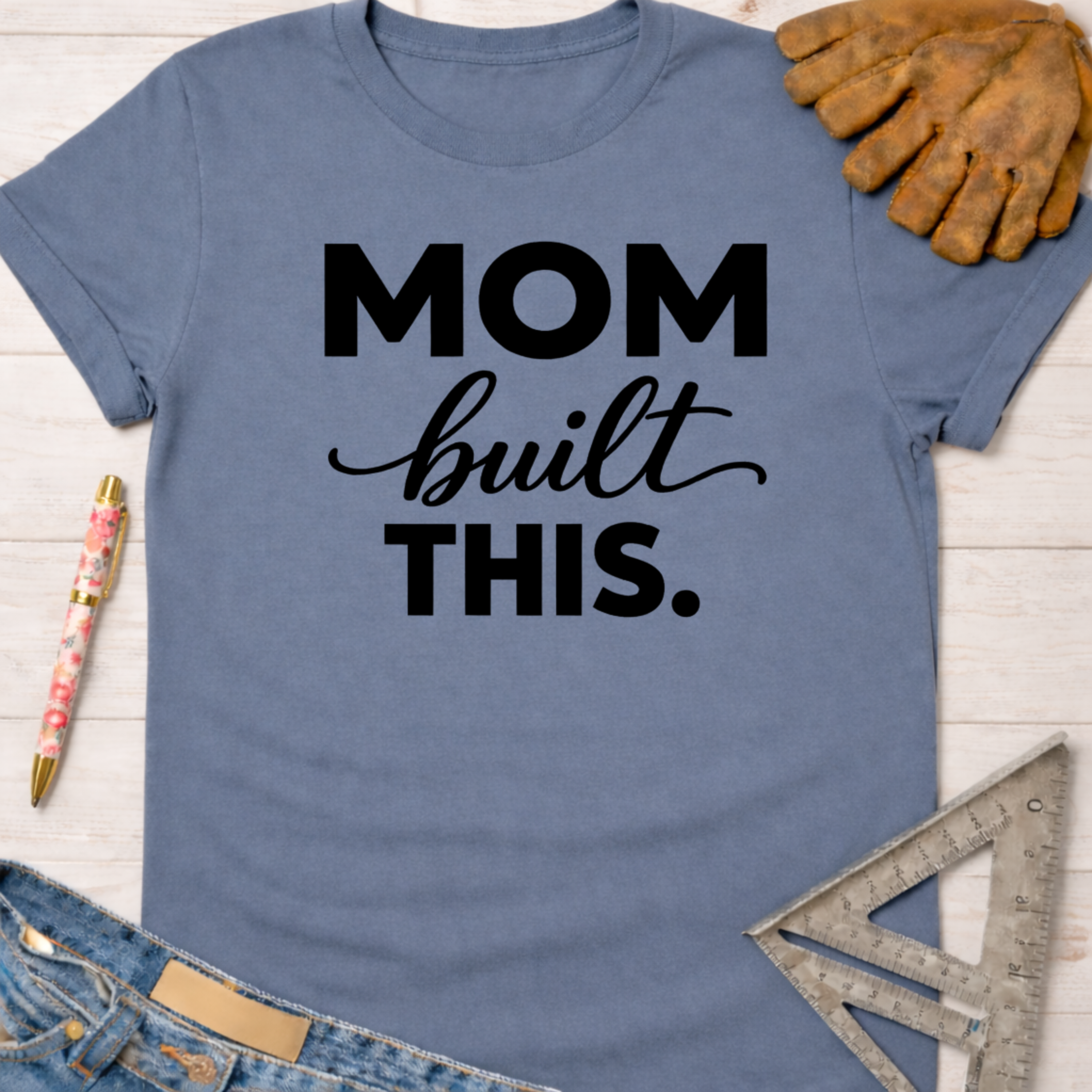 Blue "Mom built THIS." t-shirt with work gloves, jeans, and a speed square. Women's funny woodworking graphic tee shirt for female woodworkers, makers, and DIY builders — Sawdust & Ponytails