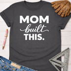 Charcoal gray "Mom built THIS." graphic tee with work glove, pen, jeans, and square ruler. Women's funny woodworking graphic tee shirt for female woodworkers, makers, and DIY builders — Sawdust & Ponytails