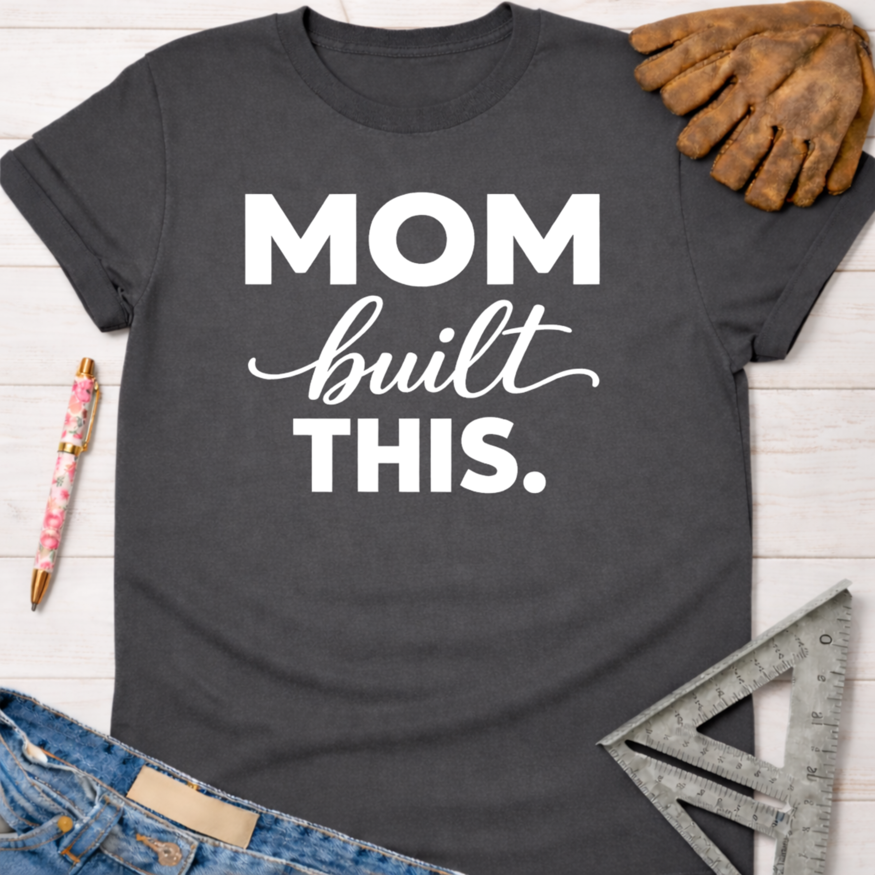 Charcoal gray "Mom built THIS." graphic tee with work glove, pen, jeans, and square ruler. Women's funny woodworking graphic tee shirt for female woodworkers, makers, and DIY builders — Sawdust & Ponytails