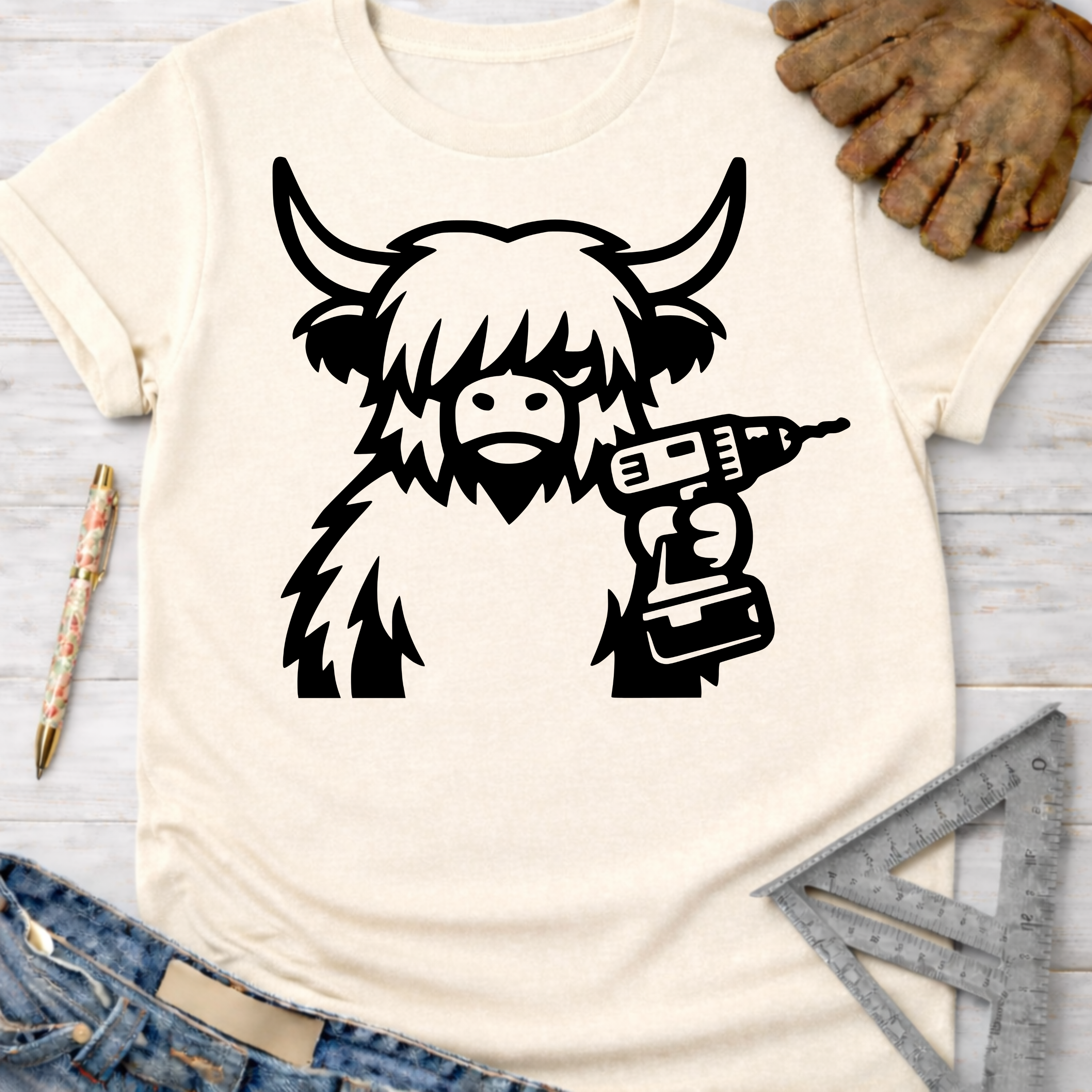 Women's funny woodworking graphic tee shirt for female woodworkers, makers, and DIY builders — Sawdust & Ponytails. Cream t-shirt with a black Highland cow holding a drill.