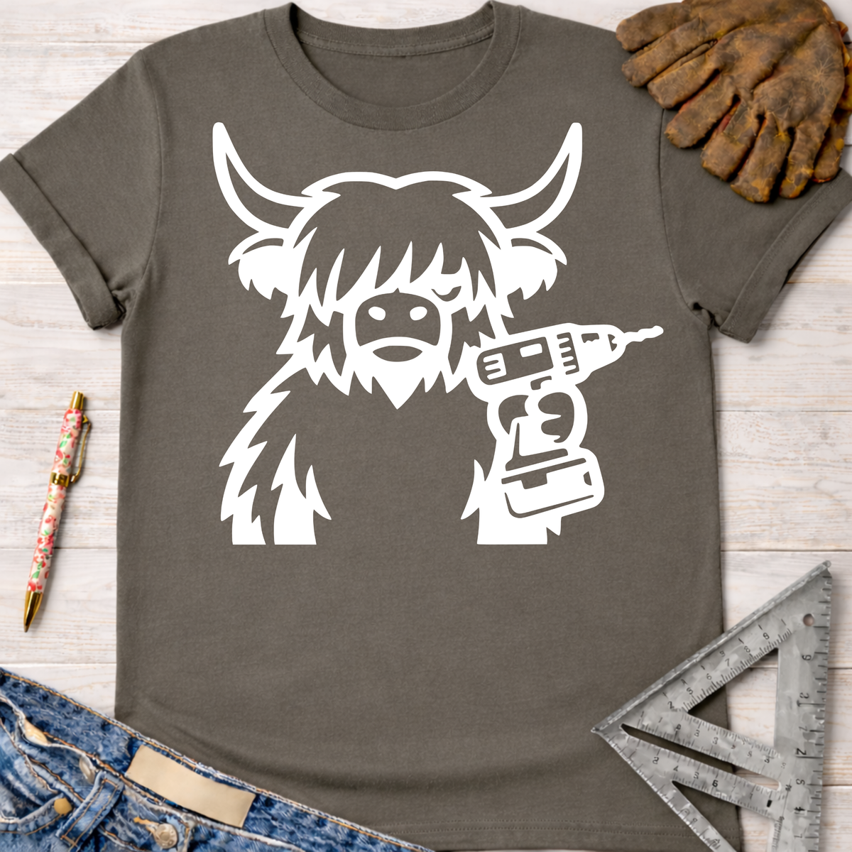 Women's funny woodworking graphic tee shirt for female woodworkers, makers, and DIY builders — Sawdust & Ponytails. Dark gray t-shirt with a white graphic of a shaggy cow holding a drill.
