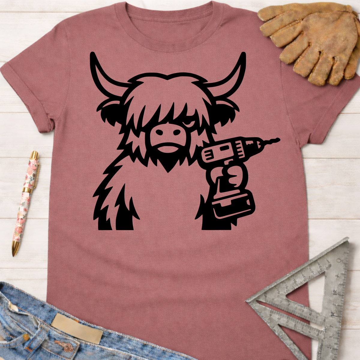 Women's funny woodworking graphic tee shirt for female woodworkers, makers, and DIY builders — Sawdust & Ponytails. Dusty rose t-shirt with a black graphic of a Highland cow holding a power drill.