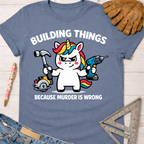 Women's funny woodworking graphic tee shirt for female woodworkers, makers, and DIY builders — Sawdust & Ponytails. Blue cotton tee with a unicorn holding a hammer, drill, and saw, text "BUILDING THINGS BECAUSE MURDER IS WRONG".