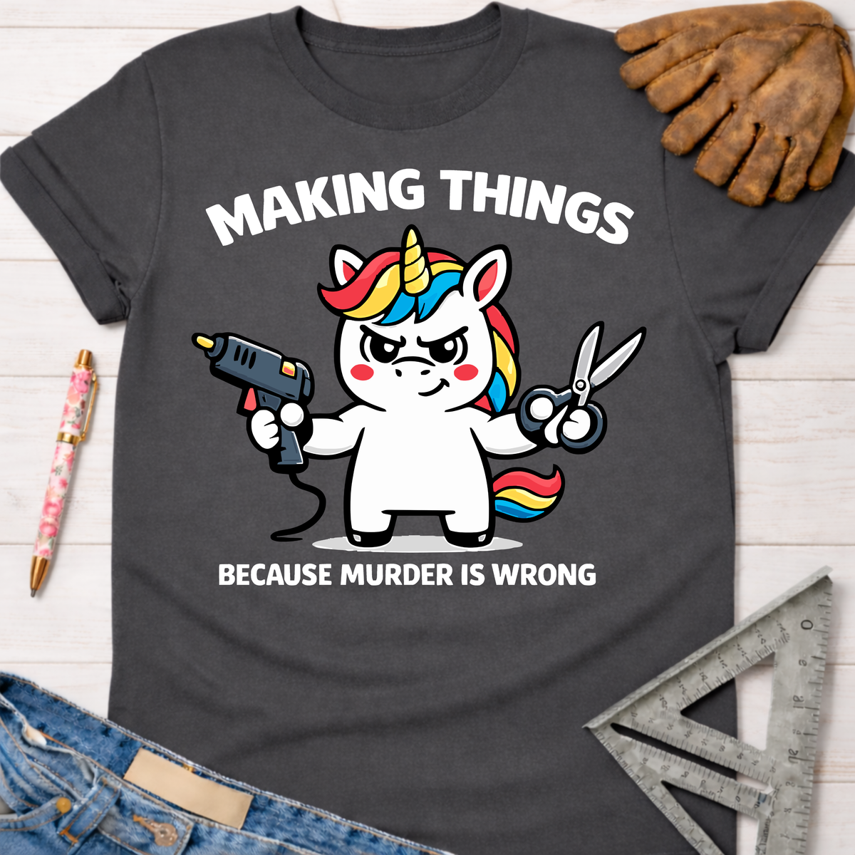 Women's funny woodworking graphic tee shirt for female woodworkers, makers, and DIY builders — Sawdust & Ponytails. Dark gray cotton tee with a cartoon unicorn holding a glue gun and scissors, text reads "MAKING THINGS BECAUSE MURDER IS WRONG".
