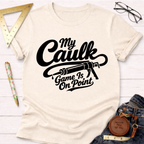 Cream "My Caulk Game Is On Point" t-shirt with black text and a caulk gun graphic, styled with jeans and tools.