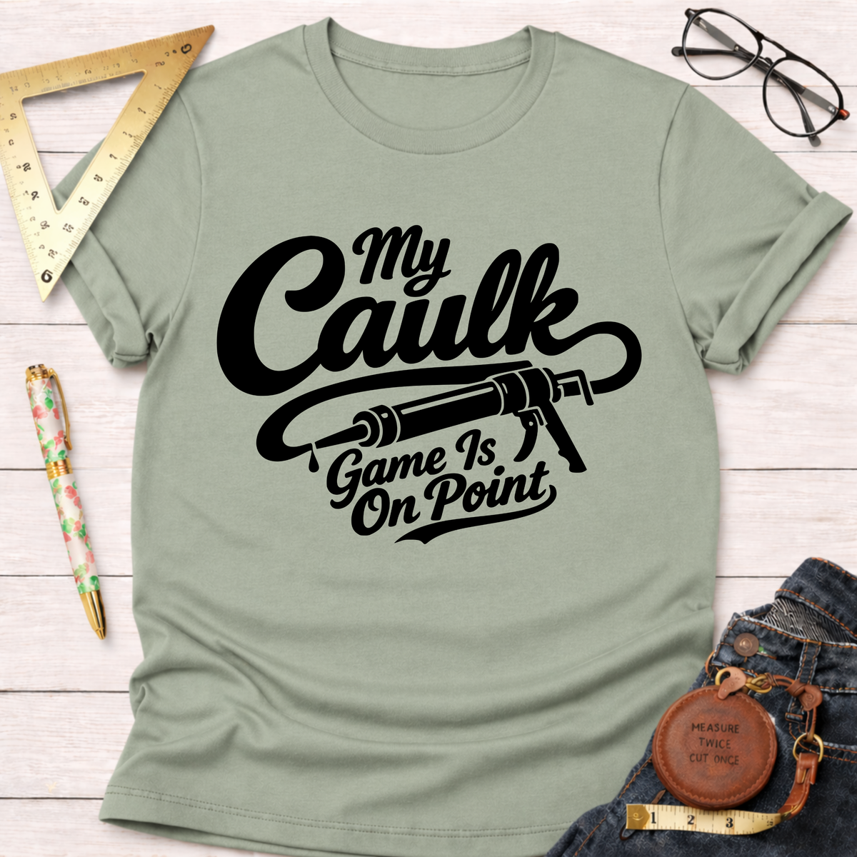 Light green cotton t-shirt with "My Caulk Game Is On Point" text and caulk gun graphic.