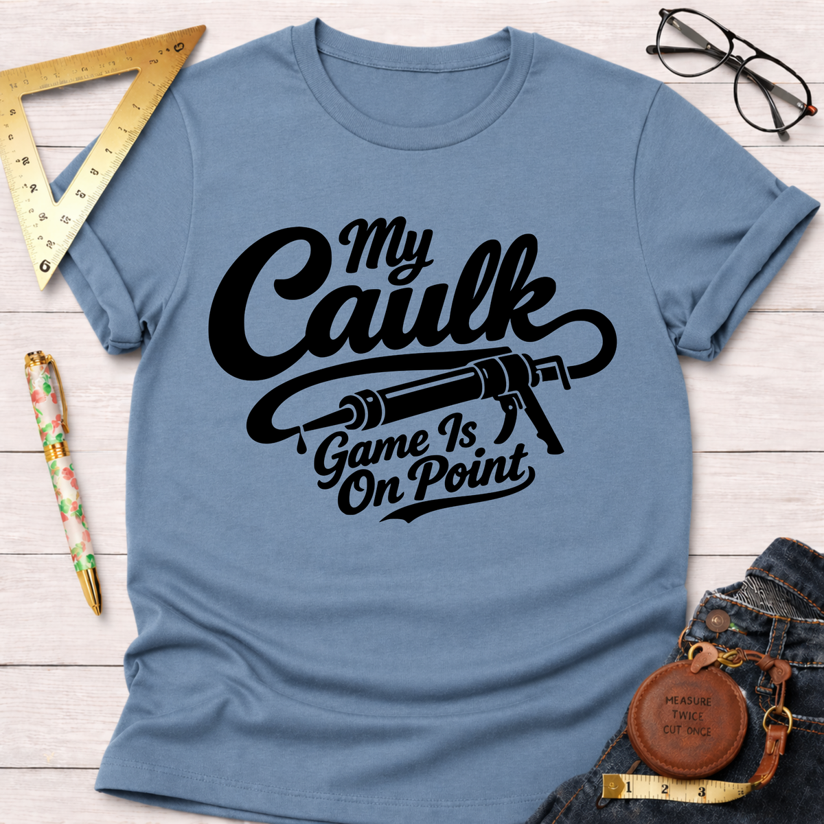 Light blue cotton t-shirt with "My Caulk Game Is On Point" graphic and a caulk gun design.