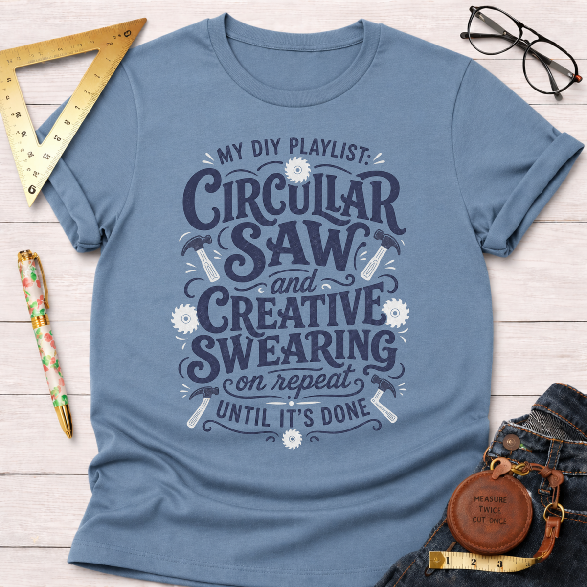 Women's funny woodworking graphic tee shirt for female woodworkers, makers, and DIY builders — Sawdust & Ponytails. Blue cotton tee with "My DIY Playlist: Circular Saw and Creative Swearing on Repeat Until It's Done" graphic.