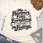 Women's funny woodworking graphic tee shirt for female woodworkers, makers, and DIY builders — Sawdust & Ponytails. Cream t-shirt with "My Hammer Fixes Everything, Including My Feelings" in black script.